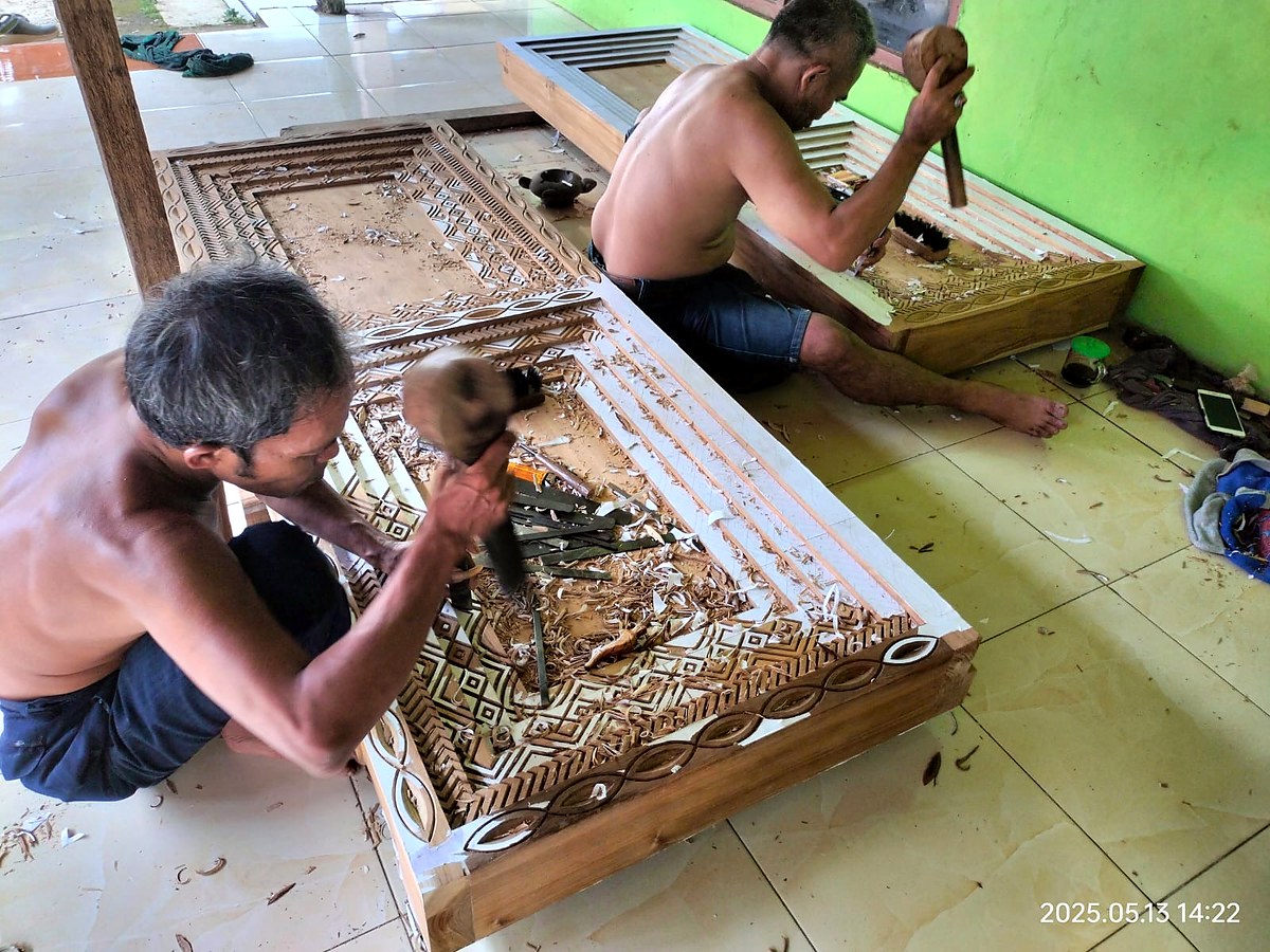 Indonesian craftsmen hand-carving wood panel